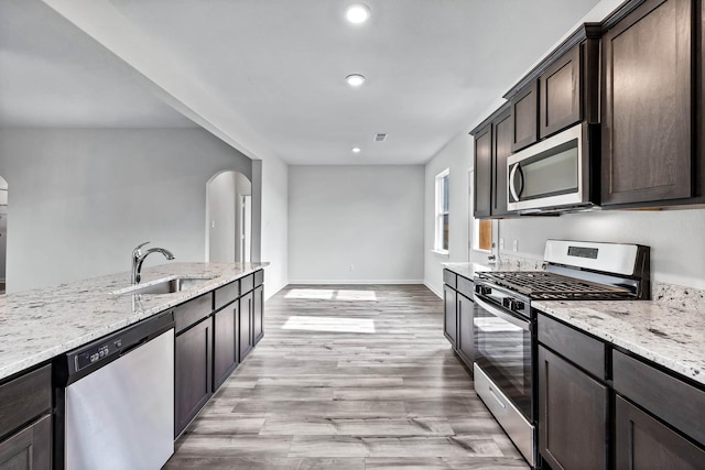 kitchen with sink, light wood-type flooring, light stone countertops, appliances with stainless steel finishes, and dark brown cabinets