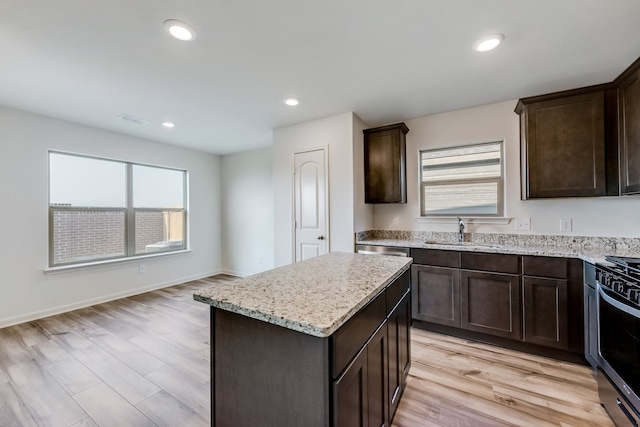 kitchen featuring light hardwood / wood-style floors, gas stove, a center island, light stone countertops, and sink