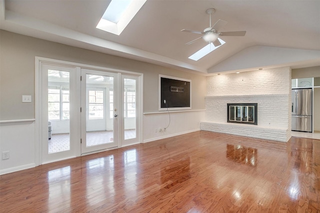 unfurnished living room featuring ceiling fan, vaulted ceiling with skylight, hardwood / wood-style flooring, and a brick fireplace