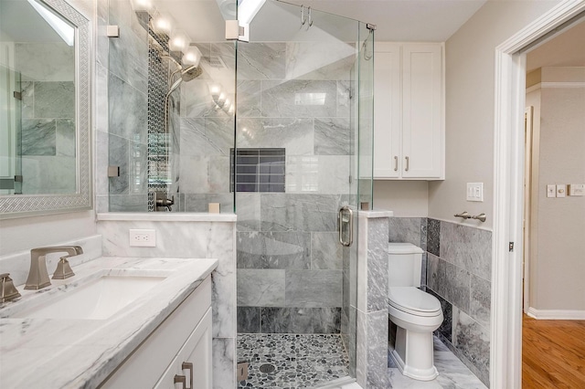 bathroom with toilet, vanity, tile walls, and a shower with door