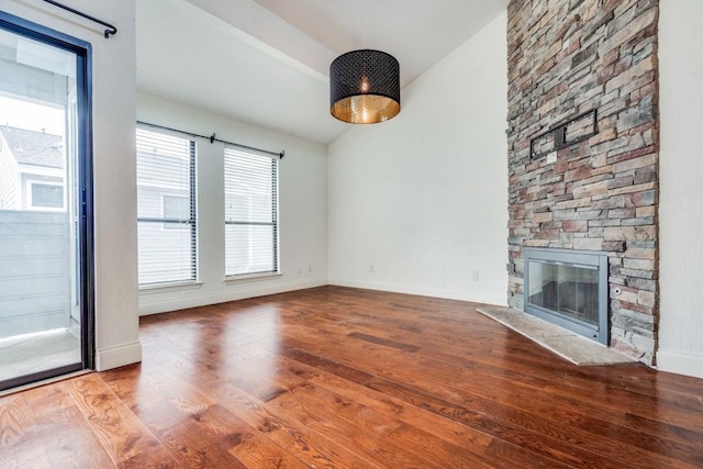 unfurnished living room featuring vaulted ceiling, hardwood / wood-style floors, and a stone fireplace