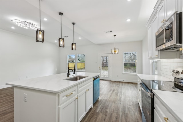 kitchen with pendant lighting, white cabinets, stainless steel appliances, sink, and a center island with sink