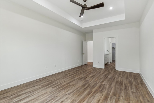 unfurnished bedroom with a spacious closet, wood-type flooring, a raised ceiling, and ceiling fan