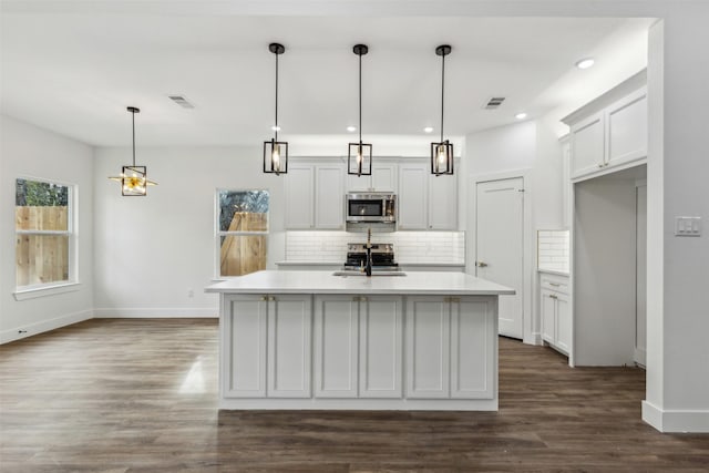 kitchen with appliances with stainless steel finishes, backsplash, a center island with sink, and hanging light fixtures