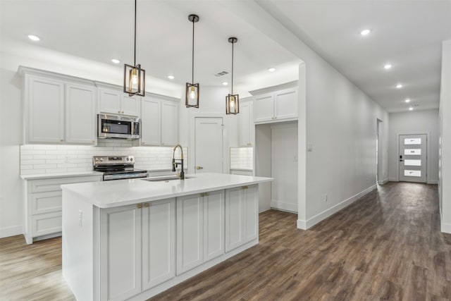 kitchen with appliances with stainless steel finishes, decorative light fixtures, sink, dark hardwood / wood-style floors, and a kitchen island with sink