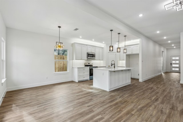 kitchen featuring appliances with stainless steel finishes, hardwood / wood-style flooring, hanging light fixtures, and a kitchen island with sink