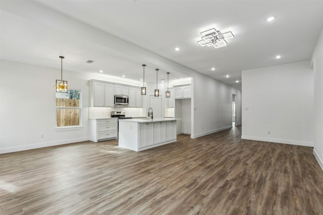 kitchen featuring hanging light fixtures, a kitchen island with sink, appliances with stainless steel finishes, and wood-type flooring