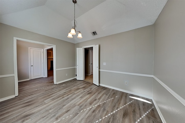 unfurnished room with wood-type flooring, a textured ceiling, a chandelier, and vaulted ceiling