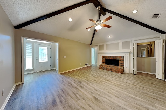 unfurnished living room featuring light hardwood / wood-style floors, a brick fireplace, ceiling fan, vaulted ceiling with beams, and a textured ceiling