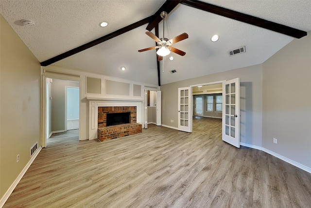 unfurnished living room featuring a textured ceiling, french doors, a fireplace, lofted ceiling with beams, and light wood-type flooring