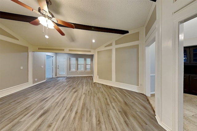 unfurnished living room featuring ceiling fan, a textured ceiling, lofted ceiling with beams, and light wood-type flooring