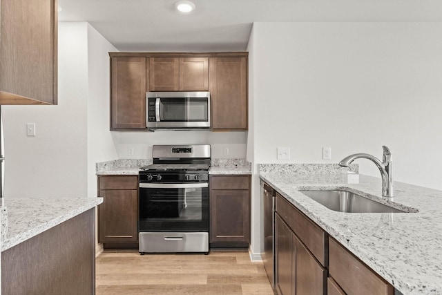 kitchen with light stone counters, sink, appliances with stainless steel finishes, and light wood-type flooring