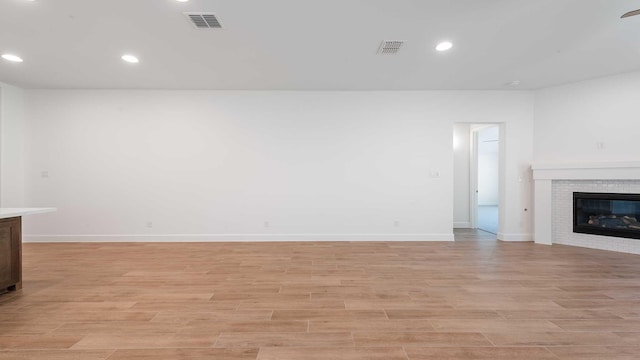 unfurnished living room featuring light wood-style floors, baseboards, a glass covered fireplace, and visible vents