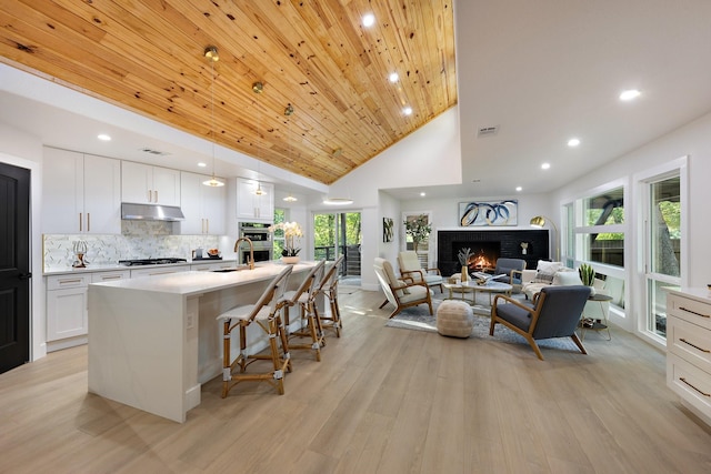 kitchen with white cabinetry, an island with sink, backsplash, a breakfast bar, and wooden ceiling