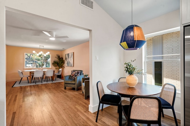 dining room with light hardwood / wood-style floors, ceiling fan with notable chandelier, vaulted ceiling, and a fireplace