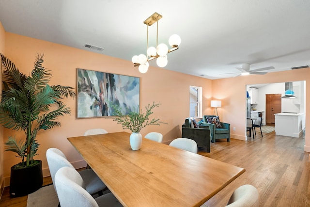 dining space with ceiling fan with notable chandelier and light hardwood / wood-style floors