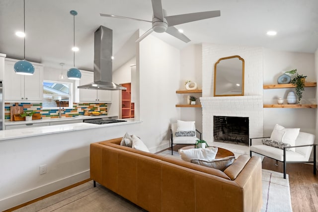 living room with ceiling fan, vaulted ceiling, a fireplace, sink, and light wood-type flooring