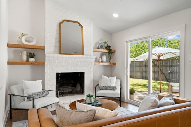 living room with vaulted ceiling, a brick fireplace, and light hardwood / wood-style floors