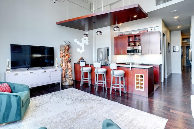 kitchen featuring decorative light fixtures, dark hardwood / wood-style floors, a center island with sink, a kitchen breakfast bar, and stainless steel appliances