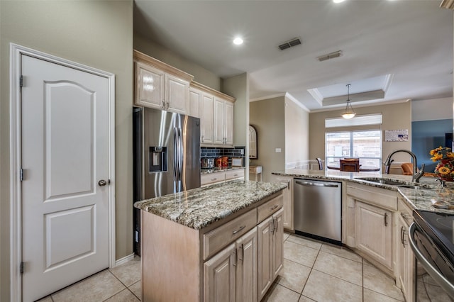 kitchen featuring decorative light fixtures, a kitchen island, sink, a tray ceiling, and appliances with stainless steel finishes