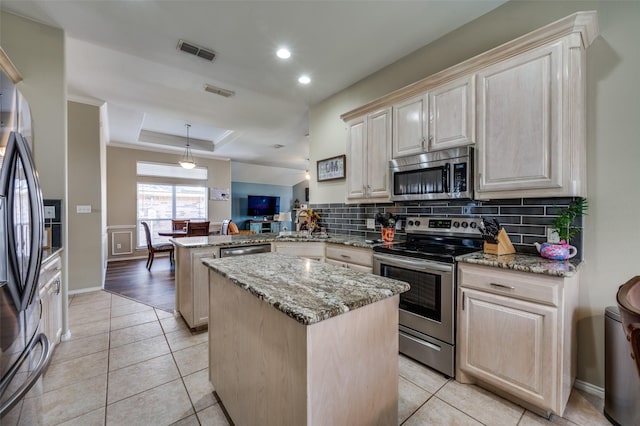 kitchen featuring light tile patterned floors, kitchen peninsula, stainless steel appliances, a tray ceiling, and a kitchen island