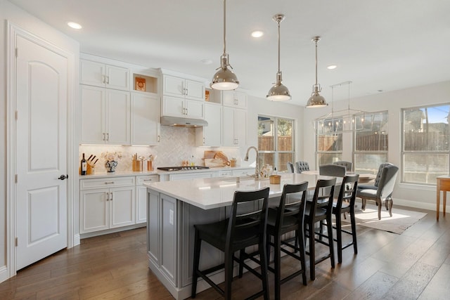 kitchen with white cabinets, decorative light fixtures, an island with sink, and dark hardwood / wood-style flooring