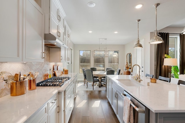 kitchen with white cabinets, pendant lighting, appliances with stainless steel finishes, a center island with sink, and sink