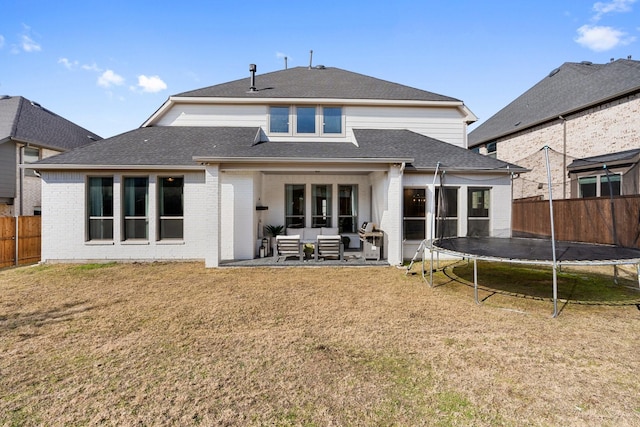 back of property with a trampoline, a yard, and a patio