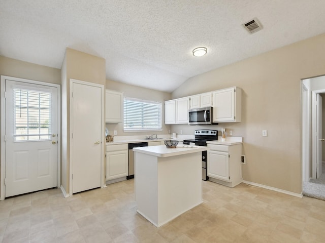 kitchen featuring appliances with stainless steel finishes, vaulted ceiling, a kitchen island, white cabinets, and sink