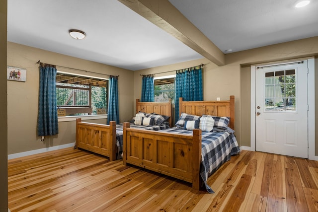 bedroom with beam ceiling, multiple windows, and light hardwood / wood-style floors