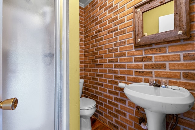 bathroom featuring toilet and brick wall