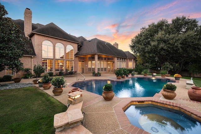 pool at dusk with a patio area, an in ground hot tub, and a yard