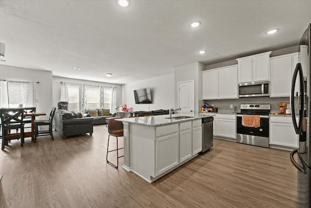 kitchen with tasteful backsplash, a center island with sink, sink, white cabinetry, and stainless steel appliances