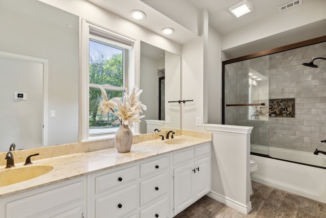 full bath featuring double vanity, bath / shower combo with glass door, a sink, and visible vents