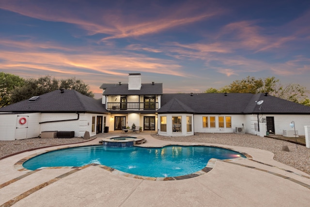 pool at dusk with a patio and a pool with connected hot tub