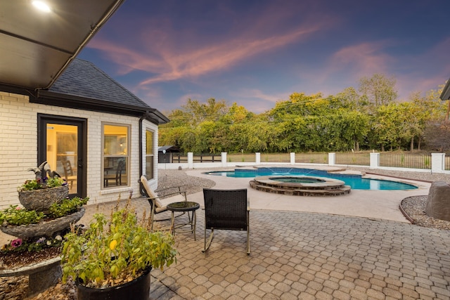 pool at dusk featuring a pool with connected hot tub, a fenced backyard, and a patio