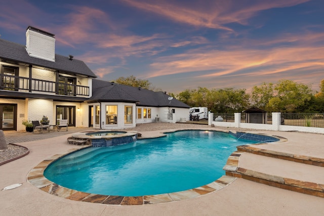 pool at dusk featuring a pool with connected hot tub, fence, and a patio