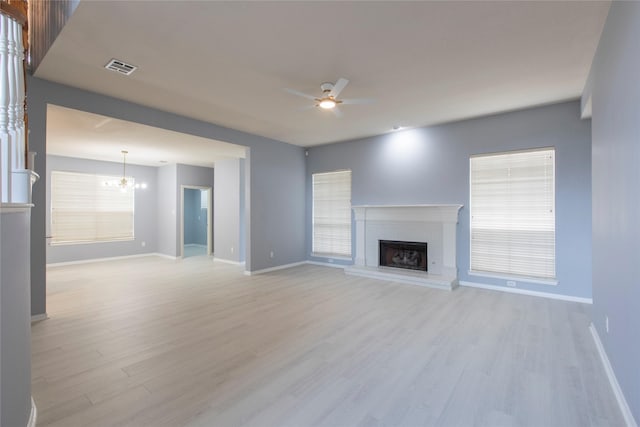 unfurnished living room featuring a fireplace, ceiling fan with notable chandelier, and light hardwood / wood-style floors