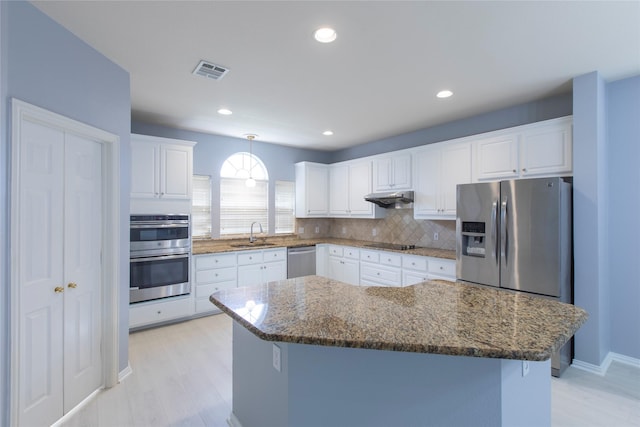 kitchen with a kitchen island, sink, stainless steel appliances, white cabinets, and dark stone counters