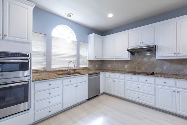 kitchen featuring white cabinetry, stainless steel appliances, decorative backsplash, dark stone counters, and sink