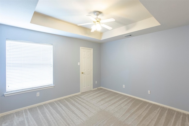 empty room featuring ceiling fan, a tray ceiling, and light carpet