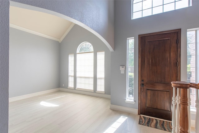 entryway featuring vaulted ceiling, ornamental molding, a healthy amount of sunlight, and light wood-type flooring