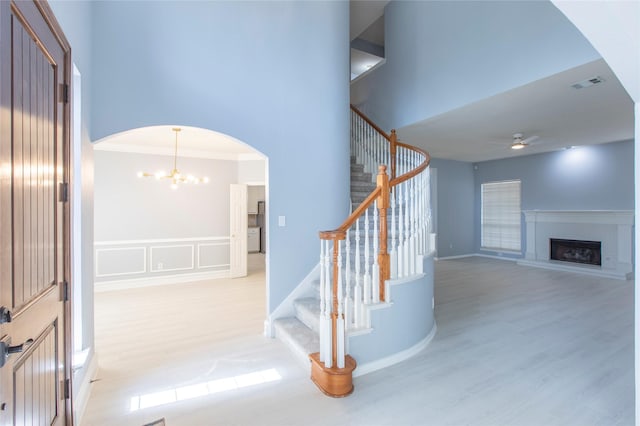 staircase with ornamental molding, ceiling fan with notable chandelier, and hardwood / wood-style flooring