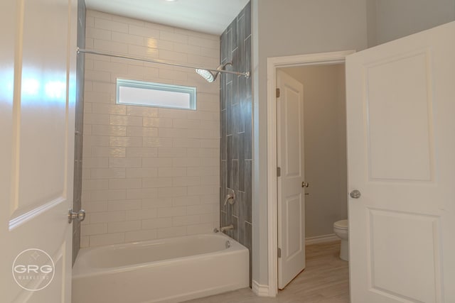 bathroom featuring wood-type flooring, toilet, and tiled shower / bath combo