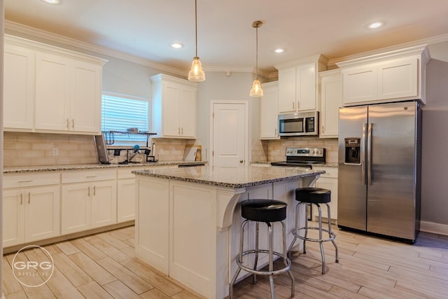 kitchen with a center island, white cabinetry, stainless steel appliances, hanging light fixtures, and crown molding