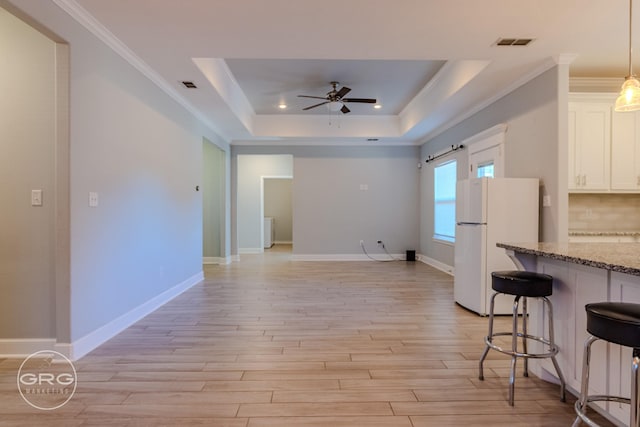 kitchen with a kitchen bar, white fridge, ceiling fan, light stone counters, and a tray ceiling