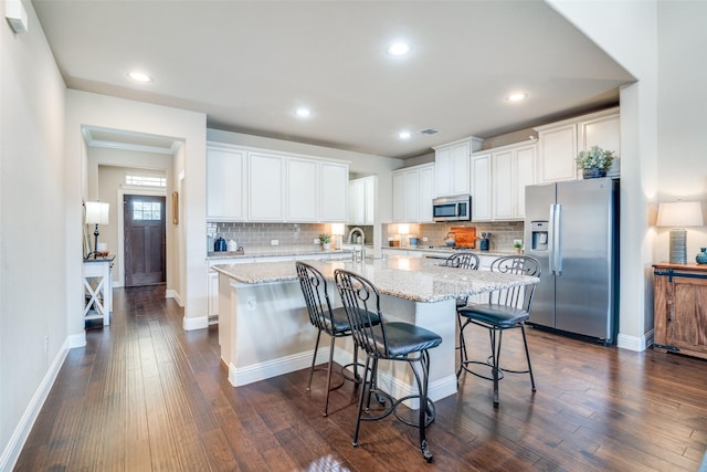 kitchen with white cabinetry, a kitchen bar, an island with sink, stainless steel appliances, and light stone counters