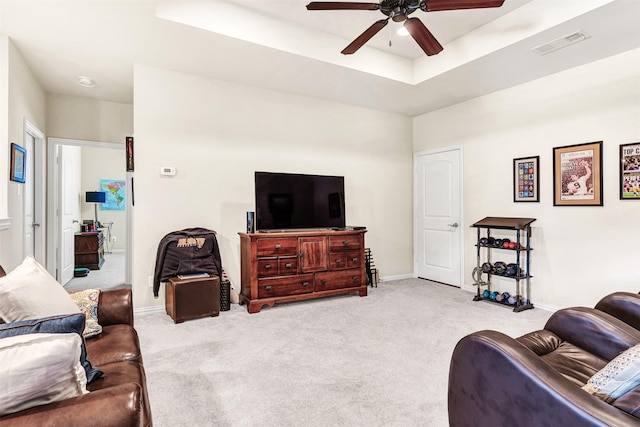 living room featuring a raised ceiling, light colored carpet, and ceiling fan