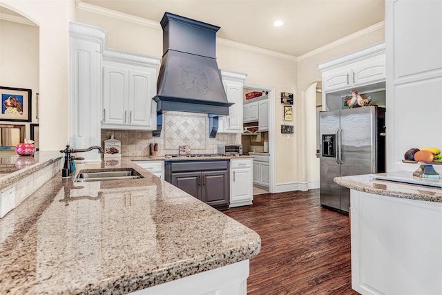 kitchen featuring sink, appliances with stainless steel finishes, custom range hood, white cabinets, and light stone counters