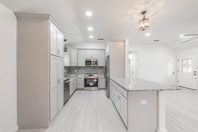 kitchen with light stone countertops, pendant lighting, stainless steel appliances, backsplash, and vaulted ceiling